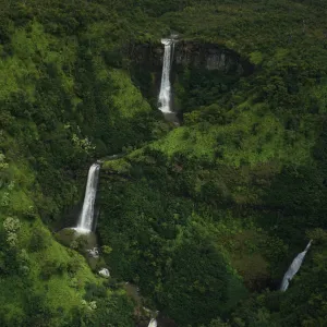three waterfalls with trees on the side of a lush green hillside