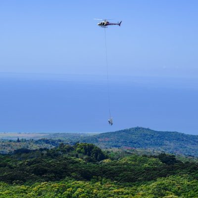 a helicopter that is flying in the sky with a sling external load over Kauai