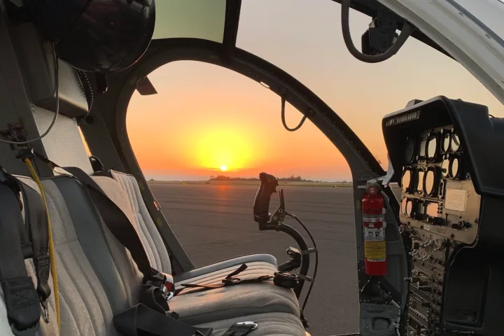 a MD 500 helicopter cockpit with no doors and sunset in background