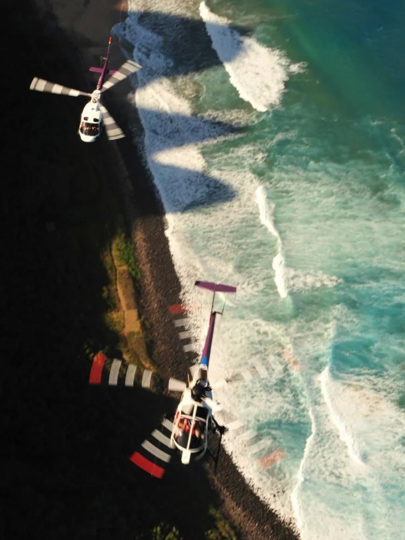 two helicopters flying over a beach