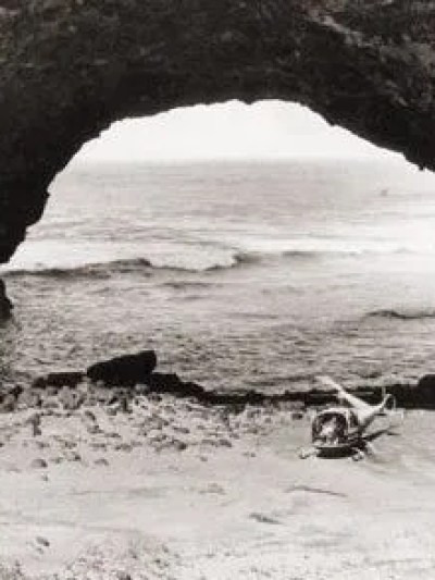 helicopter flying through rock arch over the ocean and beach