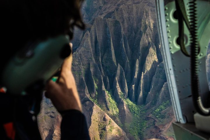 a man in doors-off helicopter looking out at Na Pali Coast