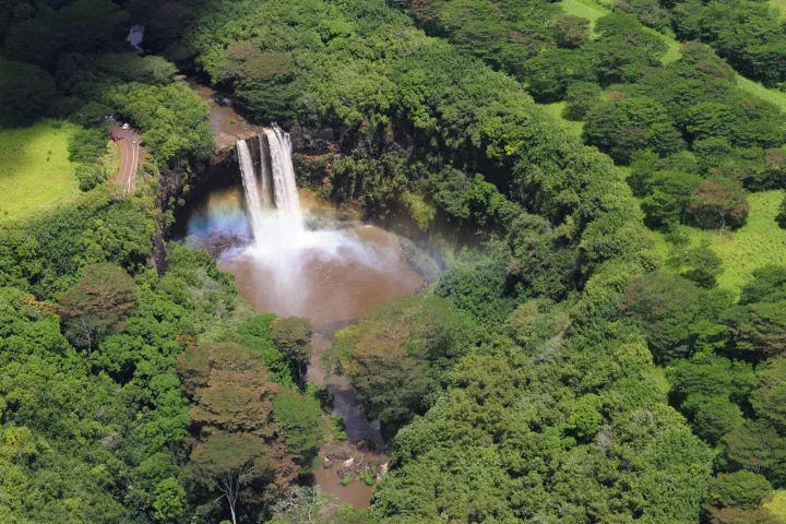 Aerial view of a waterfall with a rainbow surrounded by lush green forest.