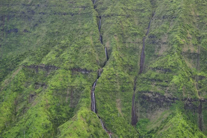 Lush green mountains with a thin waterfall cascading down and clouds above.