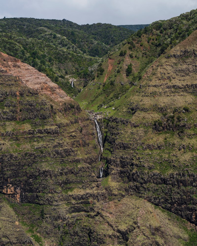 Distant waterfall cascading down a green and rocky mountain landscape.