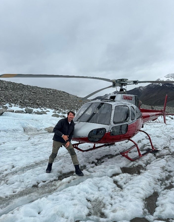 Person standing near red helicopter on snowy terrain.