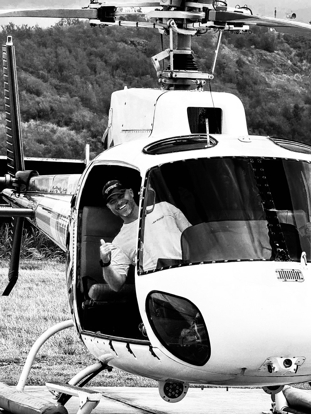 Smiling pilot giving thumbs up from helicopter cockpit, monochrome.