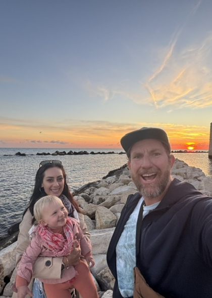 Family taking selfie on rocks by the sea during sunset.